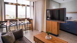 A modern living room with a sofa, a coffee table, and a TV mounted on a wooden cabinet. There is a dining area with chairs and a table, and a kitchen with cabinets and a countertop. - YalaRent Orchid Boutique Apartments (Eilat)