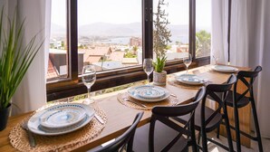 A dining table set with plates, cutlery, and glasses, with a view of a cityscape and mountains through large windows. - YalaRent Orchid Boutique Apartments (Eilat)
