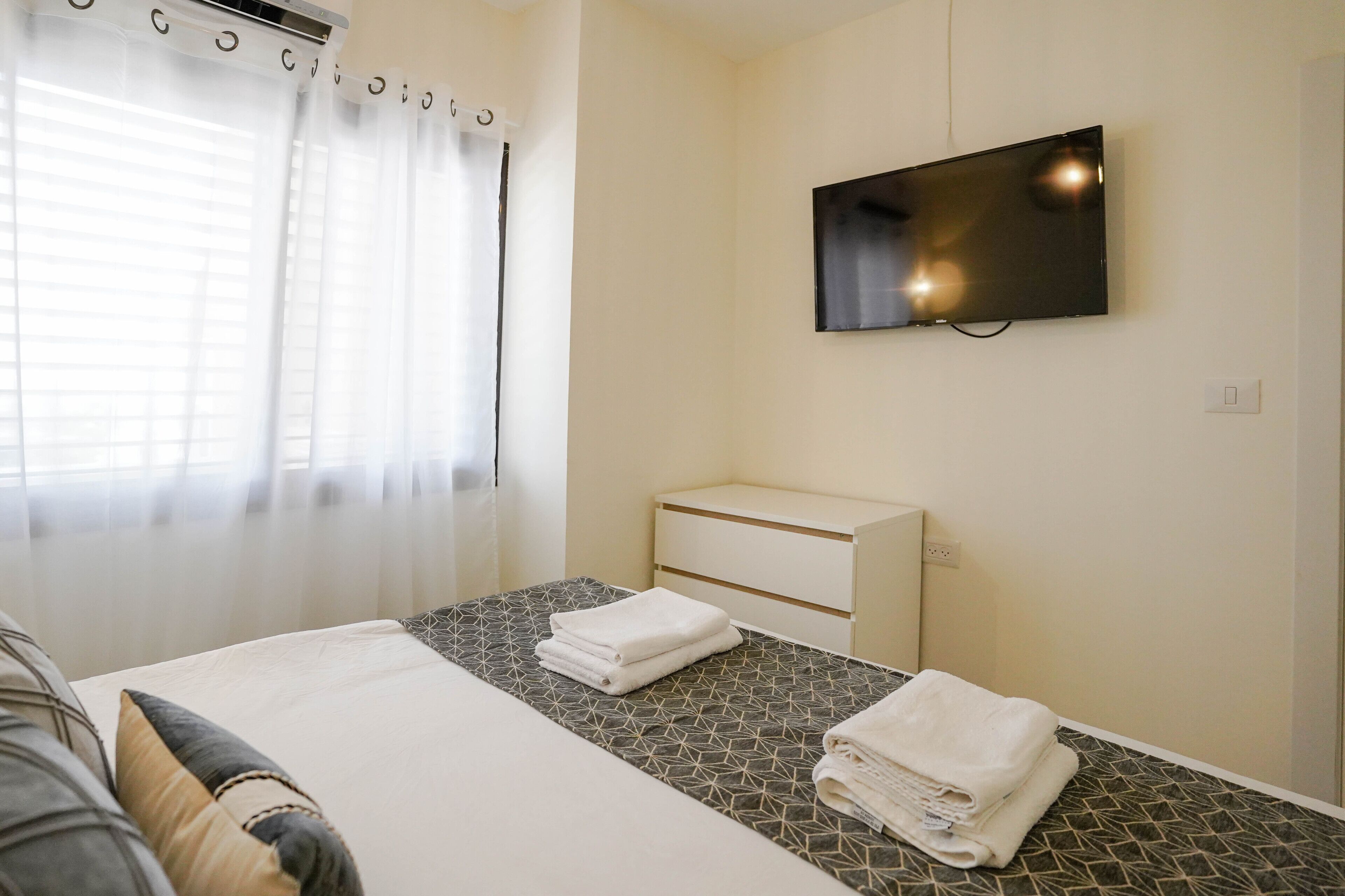 A hotel room with a bed, a TV mounted on the wall, and a window with curtains.