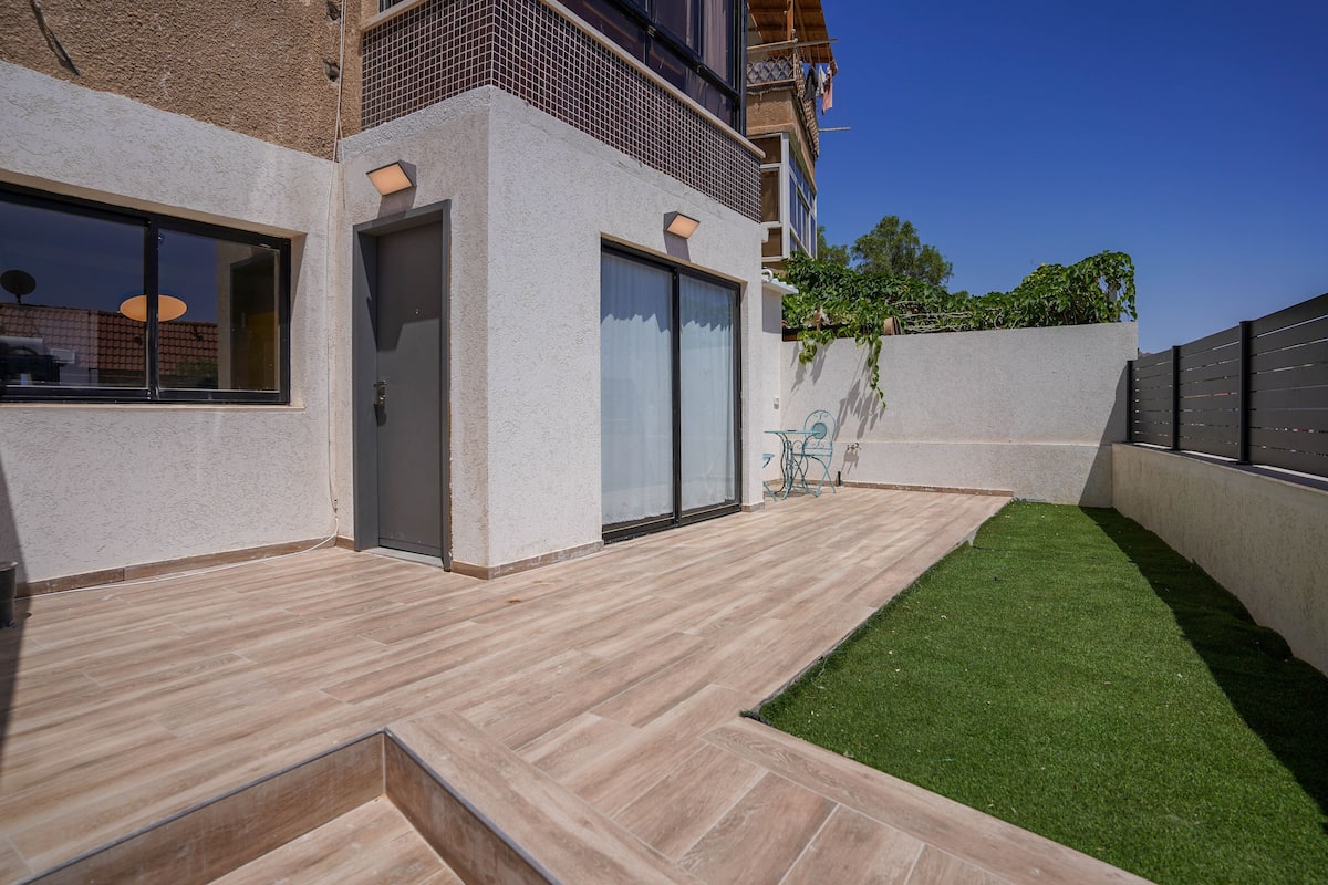 A modern building with a flat roof, large windows, and a small courtyard with artificial grass and a wooden deck.
