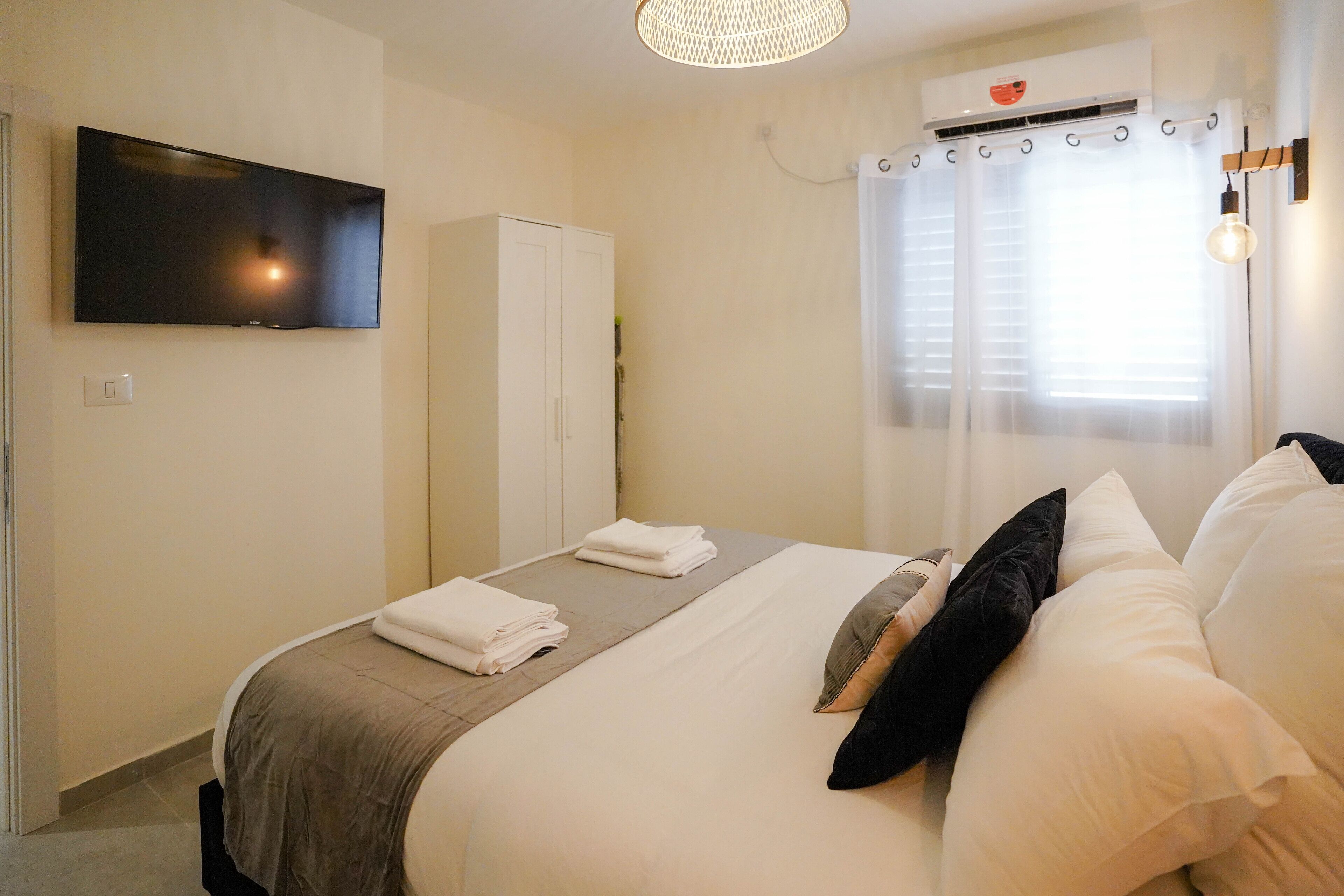A hotel room with a bed, a flat-screen TV mounted on the wall, a wardrobe, and a window with curtains.