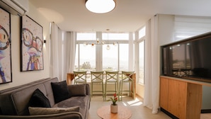 A modern living room with a sofa, a coffee table, a TV, and a dining area with chairs and a table. - YalaRent Orchid Boutique Apartments (Eilat)