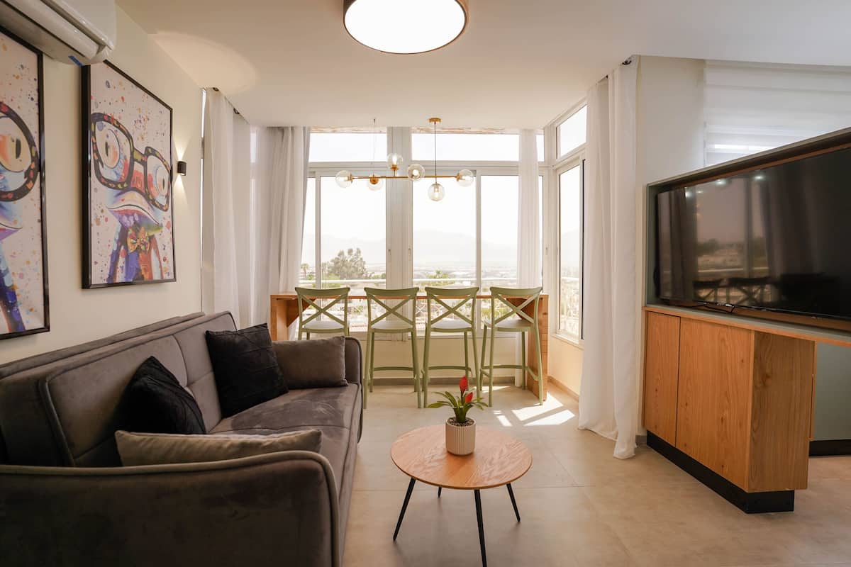 A modern living room with a sofa, a coffee table, a TV, and a dining area with chairs and a table.