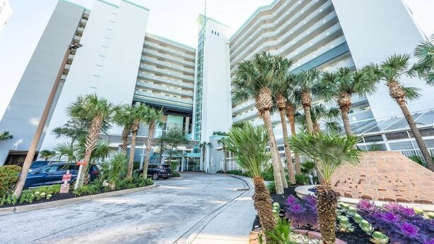 A modern hotel with a central atrium, palm trees, and a parking area. - Newly Remodeled,Dunes Village 2BR,Indoor Waterpark (Myrtle Beach)