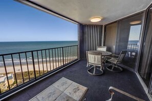 Un balcon avec vue sur l’océan, une table, deux chaises et un petit tapis.
