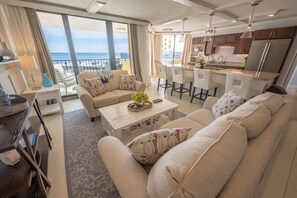 A modern living room with a sofa, coffee table, and dining area. There is a kitchen with a refrigerator and a view of the ocean. - New, Oceanview Remodeled, Private Maisons Sur Mer! (Myrtle Beach)