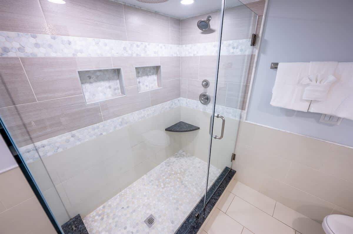 Une douche moderne avec des portes en verre, un sol carrelé et une petite étagère.