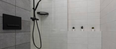 Casa de banho moderna com cabine de duche em vidro, sanita branca e pequena estante com plantas em vasos.