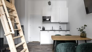 Een moderne keuken met witte kasten, een houten ladder, een houten eettafel en groene stoelen.