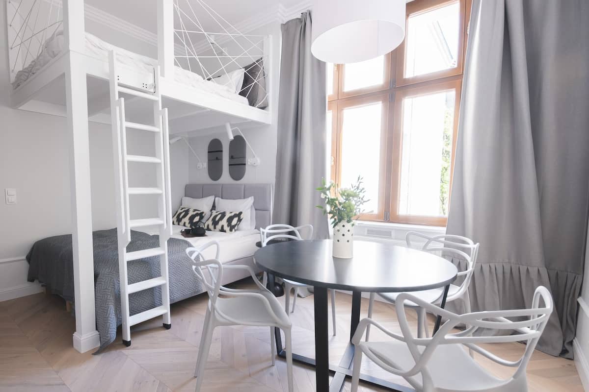 Ein modernes, kompaktes Zimmer mit Etagenbett, einem runden Esstisch mit Stühlen und einem großen Fenster mit Vorhängen.