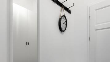Una stanza con una porta bianca, una panca bianca, un orologio a parete e una lampada a sospensione.