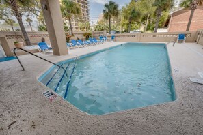 A rectangular pool with a ladder, surrounded by blue lounge chairs and palm trees.