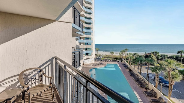 A hotel balcony with a pool, palm trees, and a view of the ocean. - Experience a Coastal Paradise,  Breathtaking Views (Myrtle Beach)