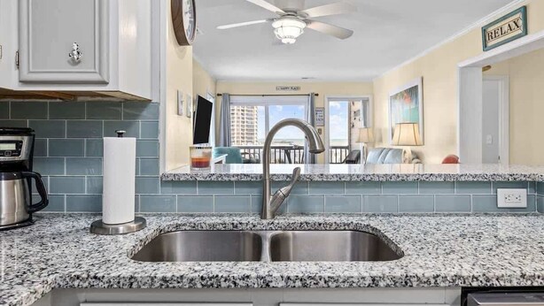 A kitchen with granite countertops, a stainless steel sink, and a ceiling fan.