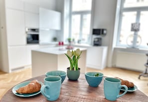 Une table en bois dressée pour le petit-déjeuner, avec des croissants, des tasses bleues et une plante en pot.