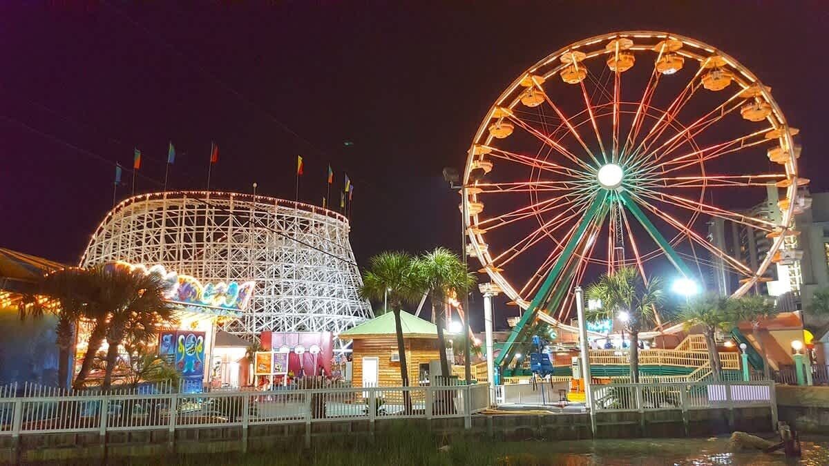 A Ferris wheel and a roller coaster at a nighttime amusement park.