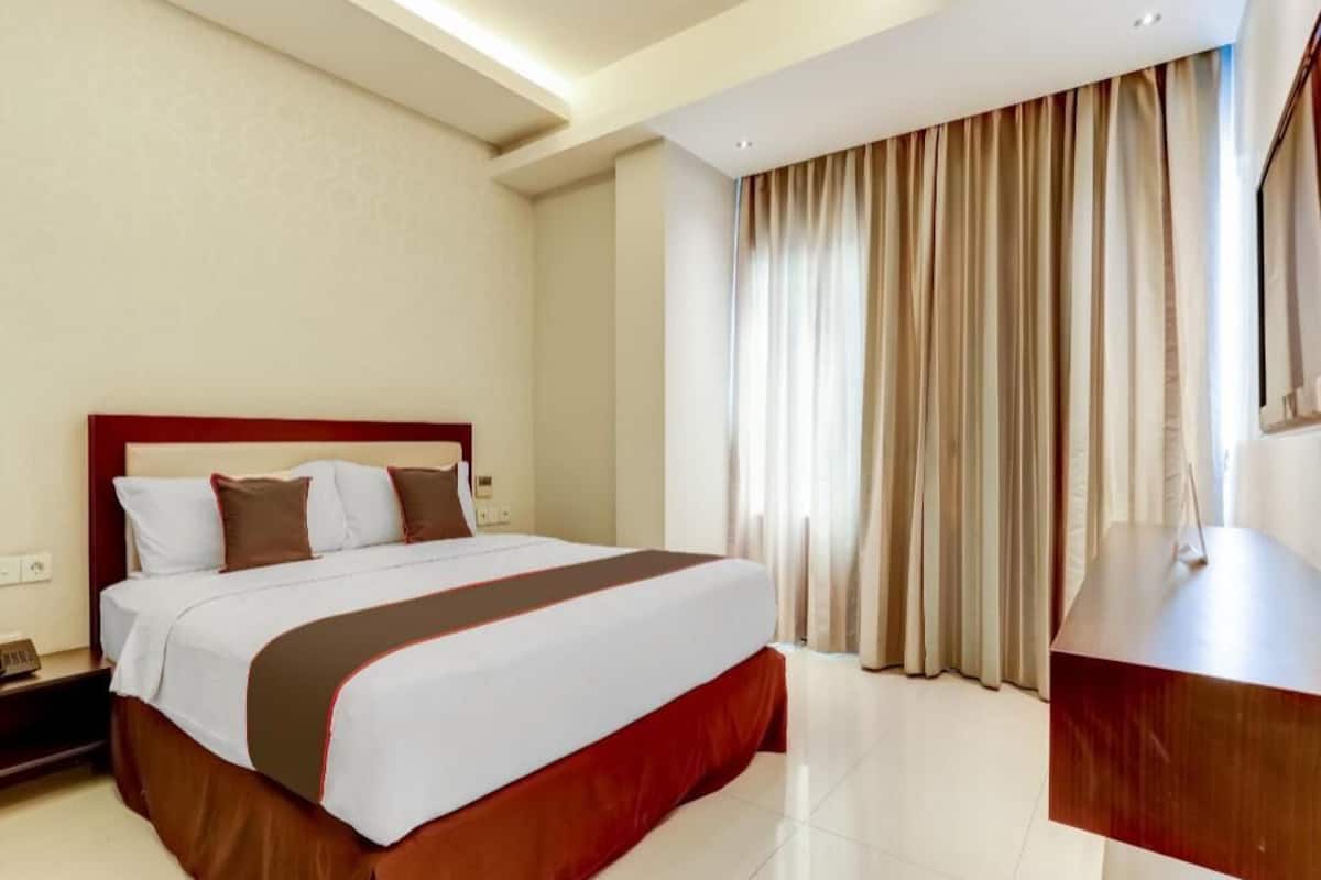 Habitació d'hotel amb un llit gran, una taula de treball i una finestra amb cortines.