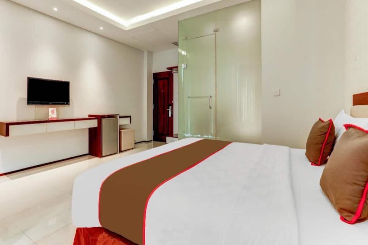 Habitació d'hotel moderna amb un llit gran, televisió de pantalla plana, escriptori i porta de vidre que dona a un bany.