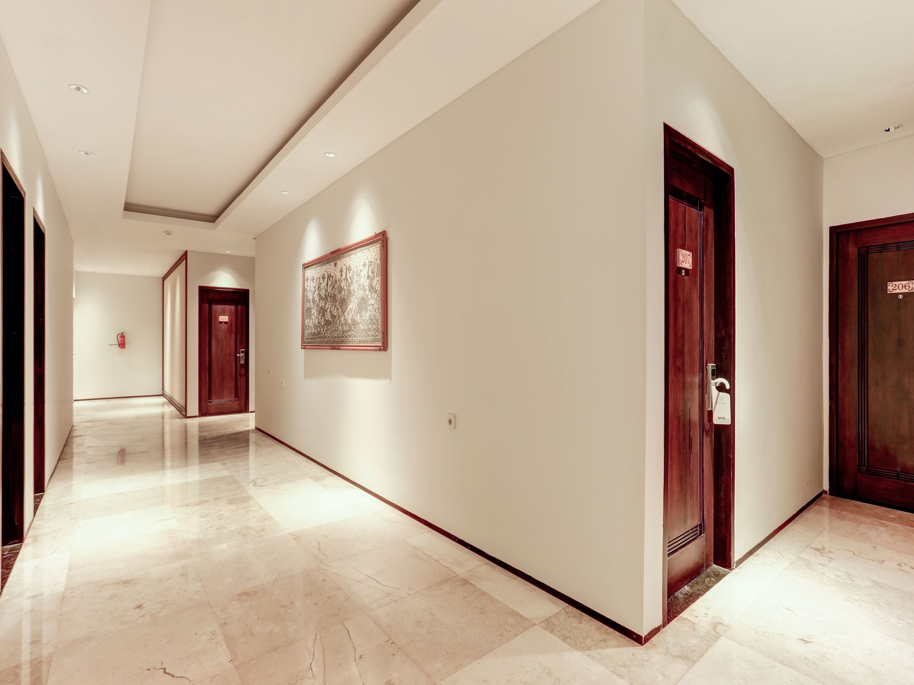 A modern hotel corridor with marble floors, wooden doors, and a framed artwork on the wall.