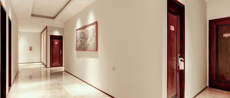 A modern hotel corridor with marble floors, wooden doors, and a framed artwork on the wall.