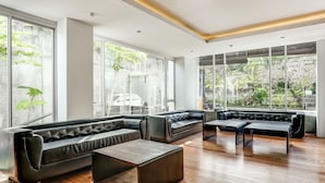A modern lounge with leather sofas, wooden flooring, and large windows offering a view of greenery. - Collection O Legian Near Pantai Kuta Formerly Premium Legian (Legian)