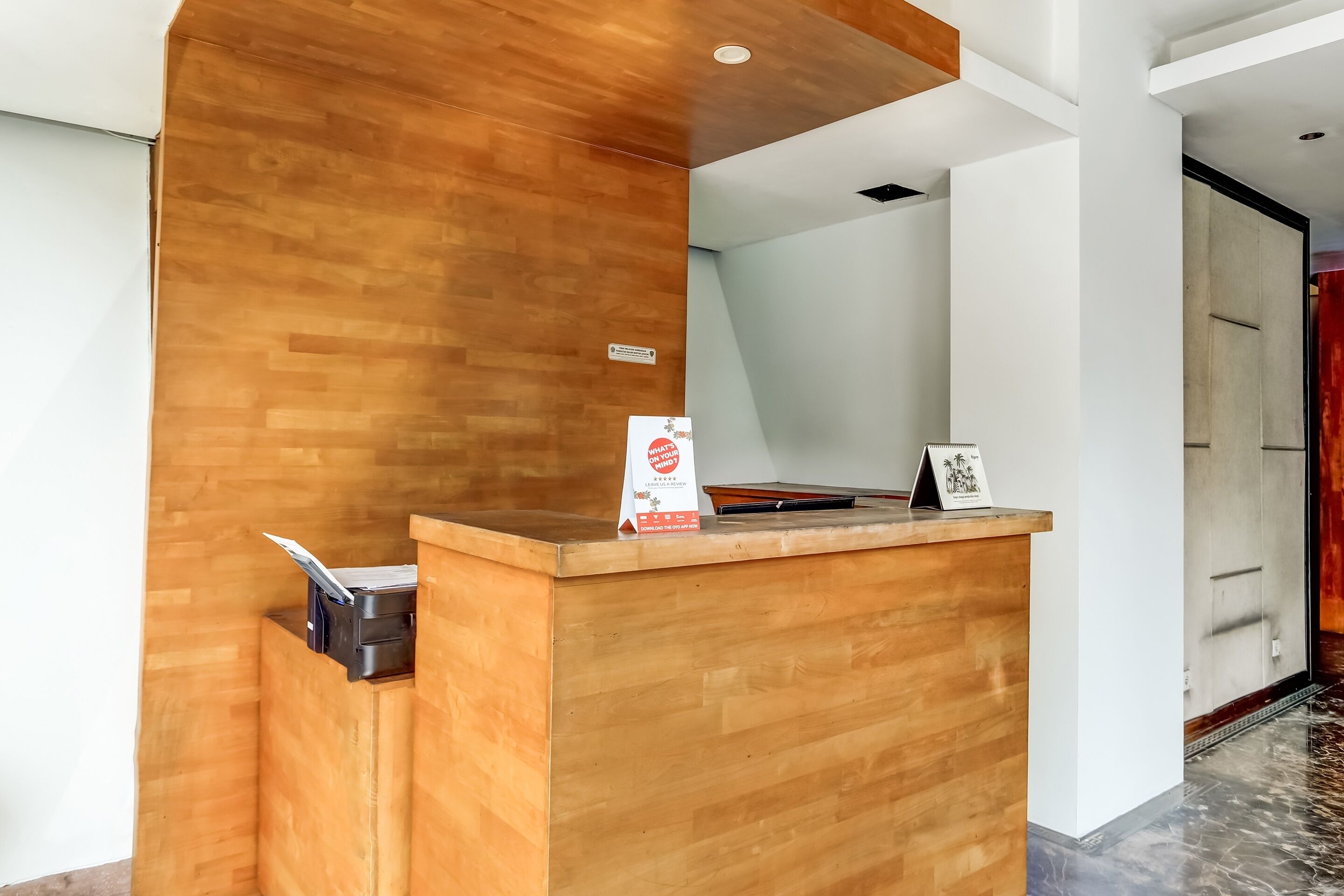 A reception desk with a wooden finish, a signboard, and a black trash bin.