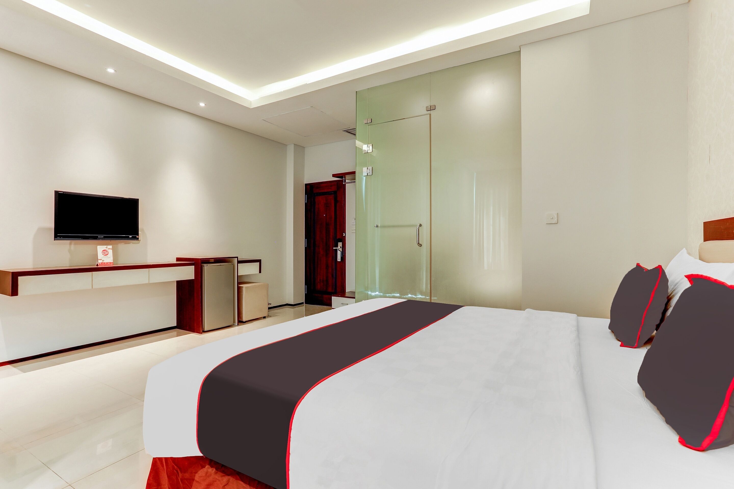 A modern hotel room with a large bed, a flat-screen TV, a desk, and a glass door closet.