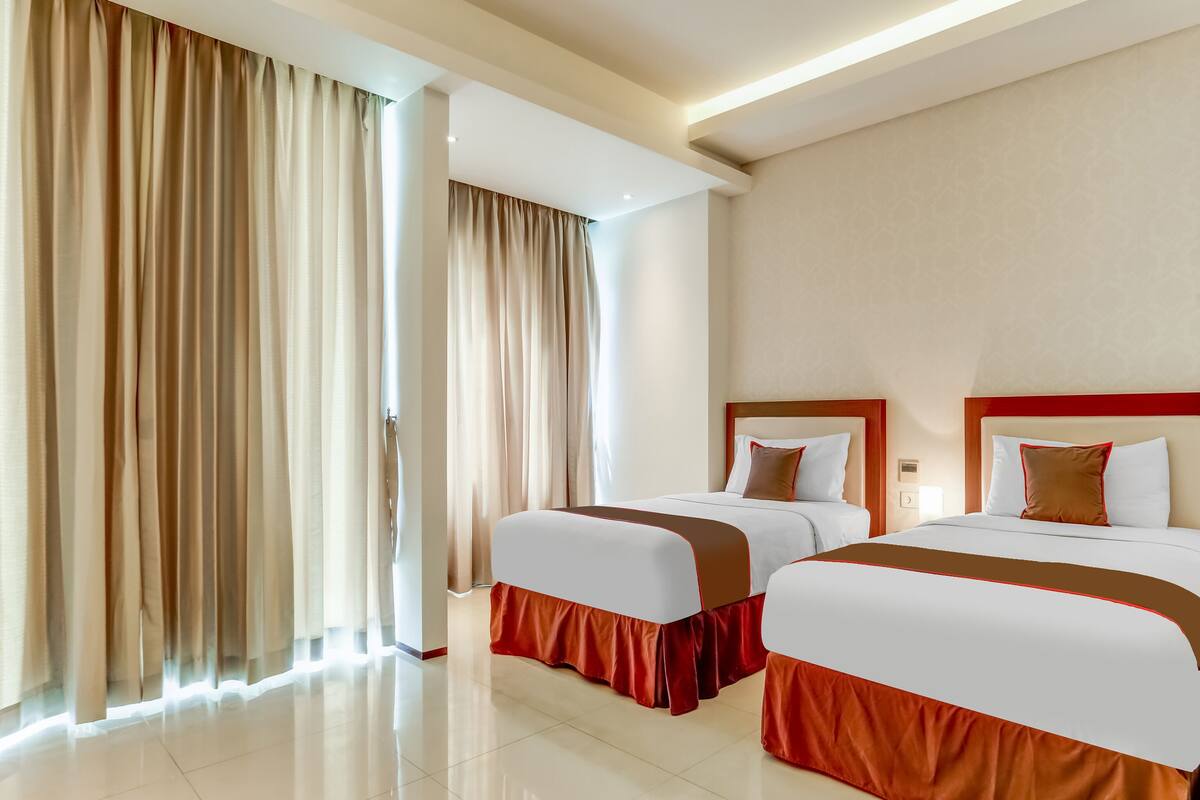 Habitació d'hotel amb dos llits, parets beix i una finestra gran amb cortines.