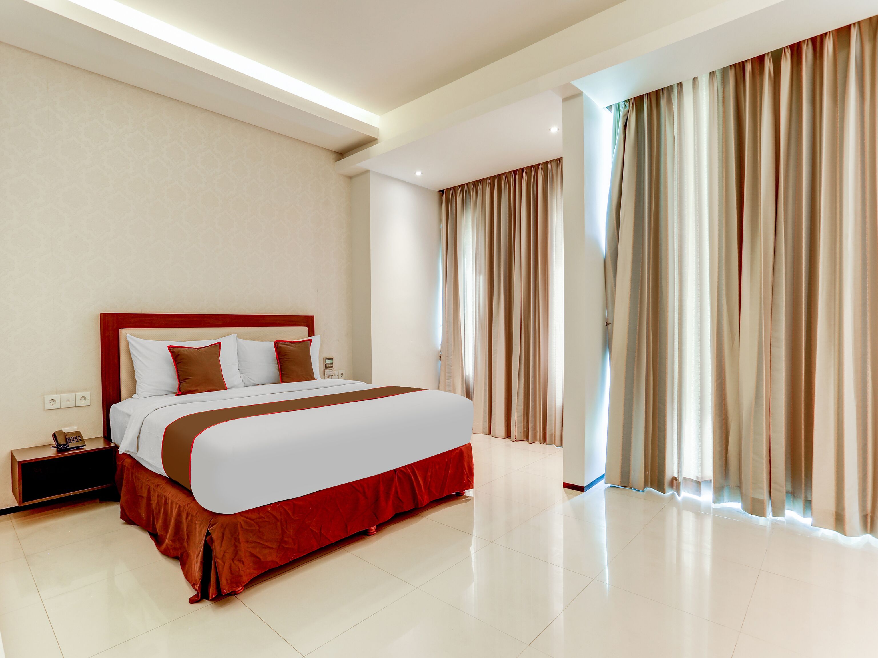 Habitació d'hotel amb un llit gran, una tauleta de nit i una finestra amb cortines.