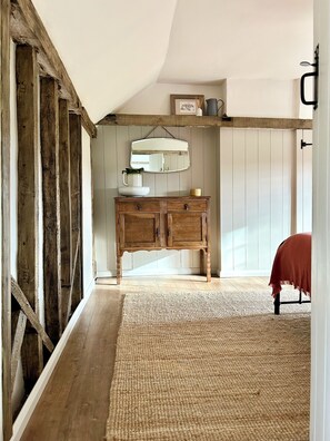 A room with a wooden floor, a woven rug, a wooden cabinet with a mirror, and a bed with a red cover. - Cosy country cottage with lots of local walks, and short drive into Woodbridge (Hasketon)