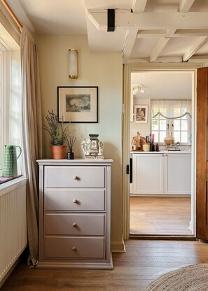 A room with a wooden floor, a white dresser with drawers, a framed picture on the wall, and a window with curtains.