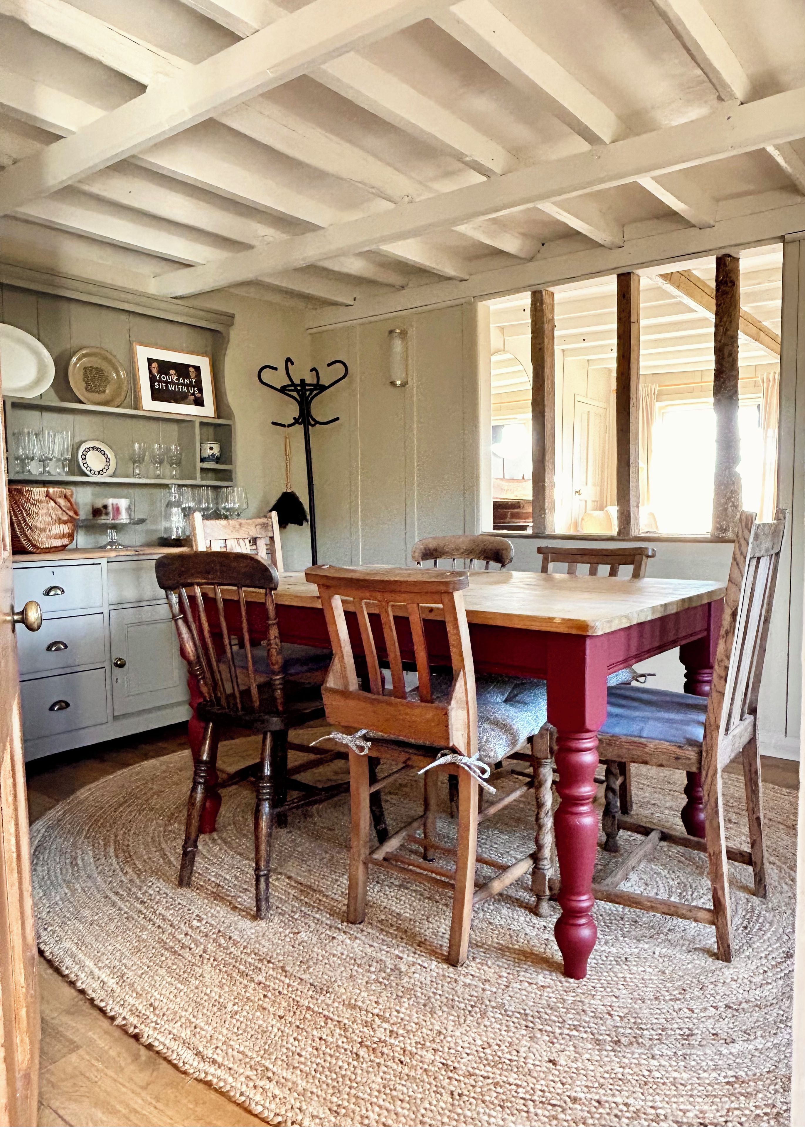 A dining area with a wooden table and chairs, a woven rug, and a coat rack.