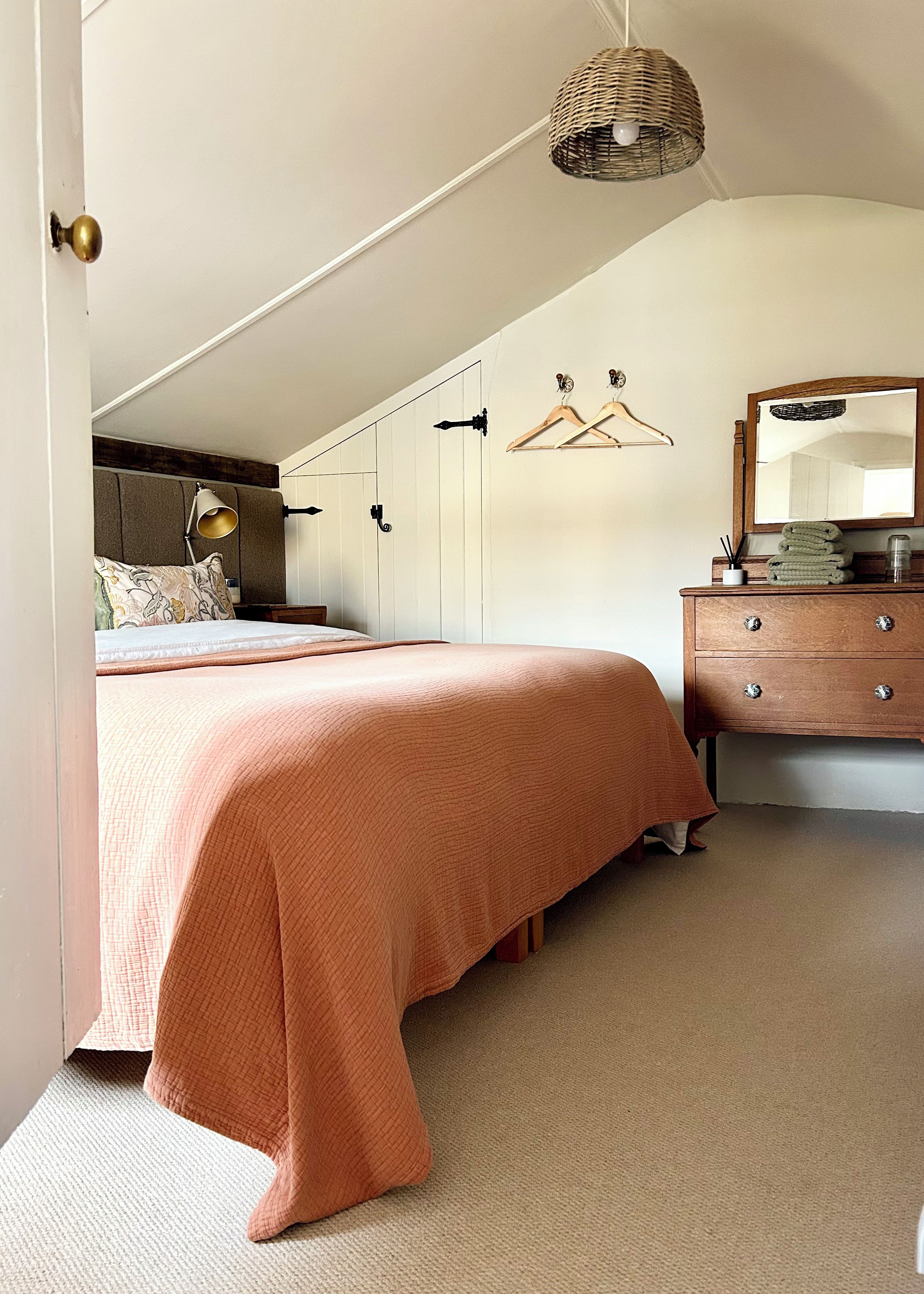 A bedroom with a bed, dresser, hanging clothes rack, and a wall-mounted mirror.