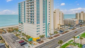 Un hotel de varios pisos con balcones, cerca de una playa y una calle con coches aparcados.