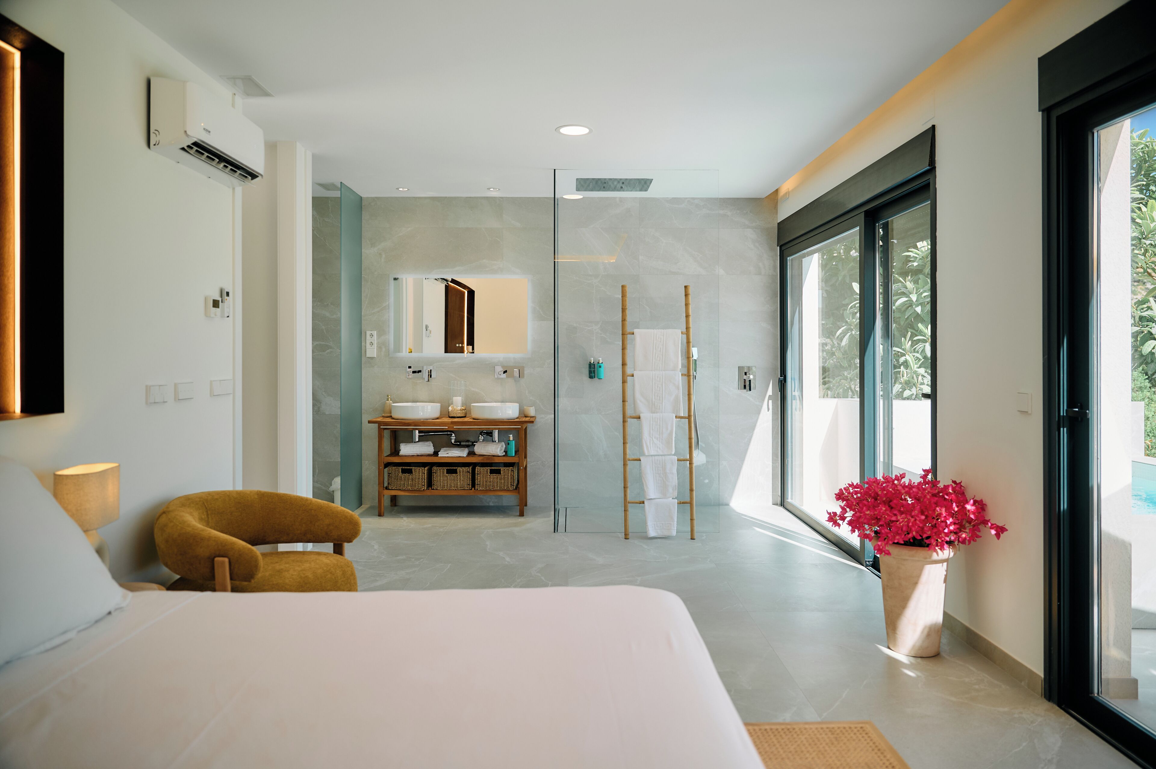 Habitación de hotel moderna con cama, baño con espejo grande, ducha y vista a zonas verdes por las ventanas.