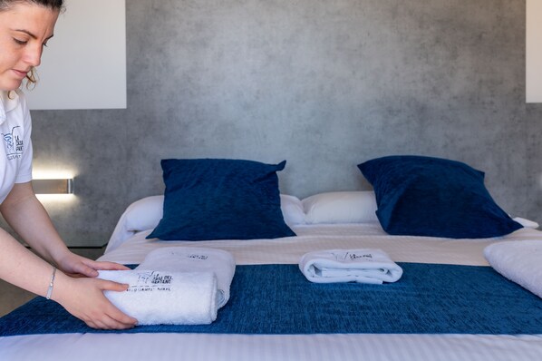 A neatly made bed with blue and white bedding, a folded towel, and a person adjusting the bed. - YOUNG Hotels Denia (La Vall de Laguar)