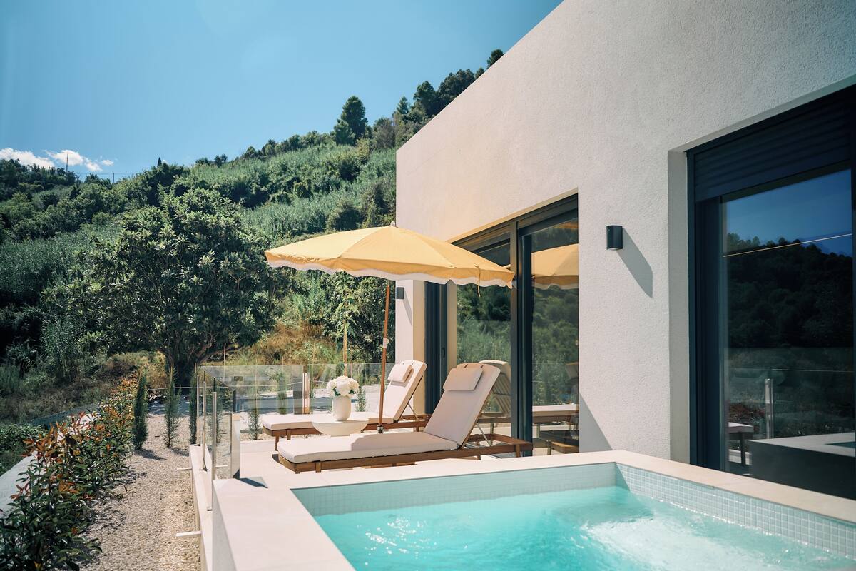 A modern outdoor pool area with lounge chairs and umbrellas, surrounded by a hillside.