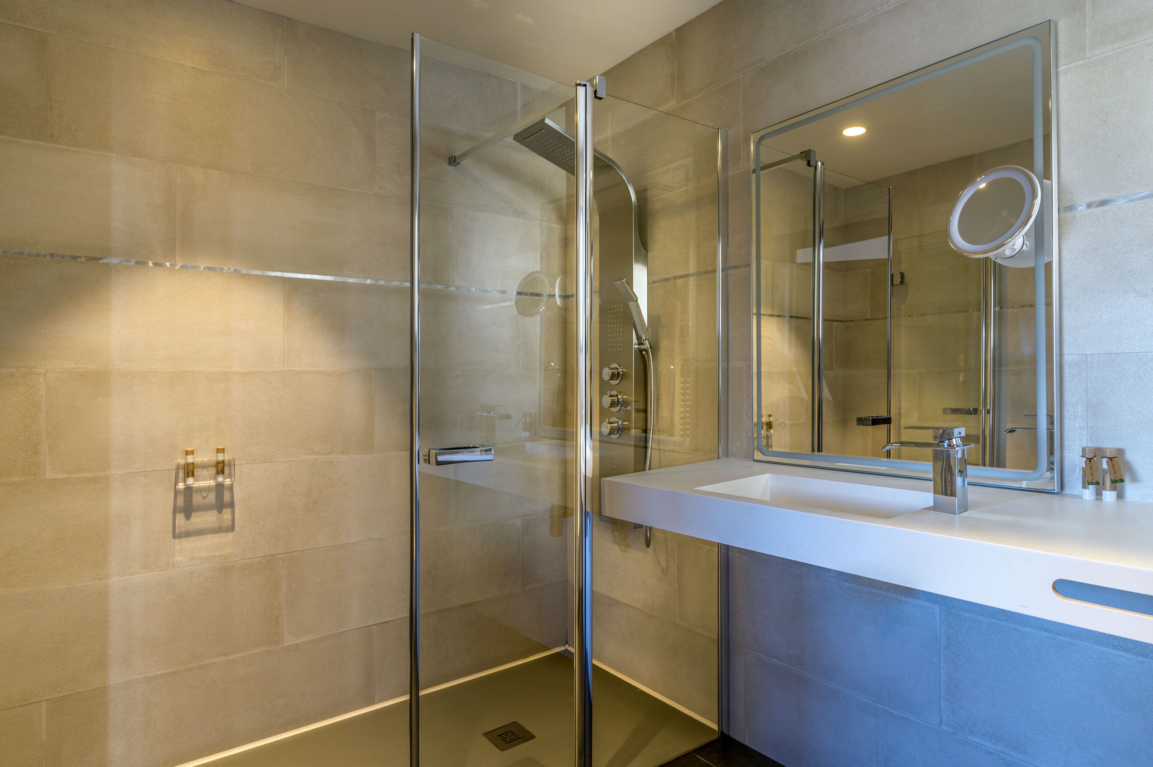 Un baño moderno con ducha de vidrio, un espejo grande y un lavamanos blanco.