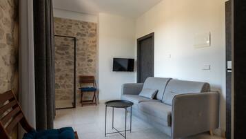 Una sala de estar moderna con un sofá gris, una mesita redonda, una silla de madera y un televisor montado en la pared.