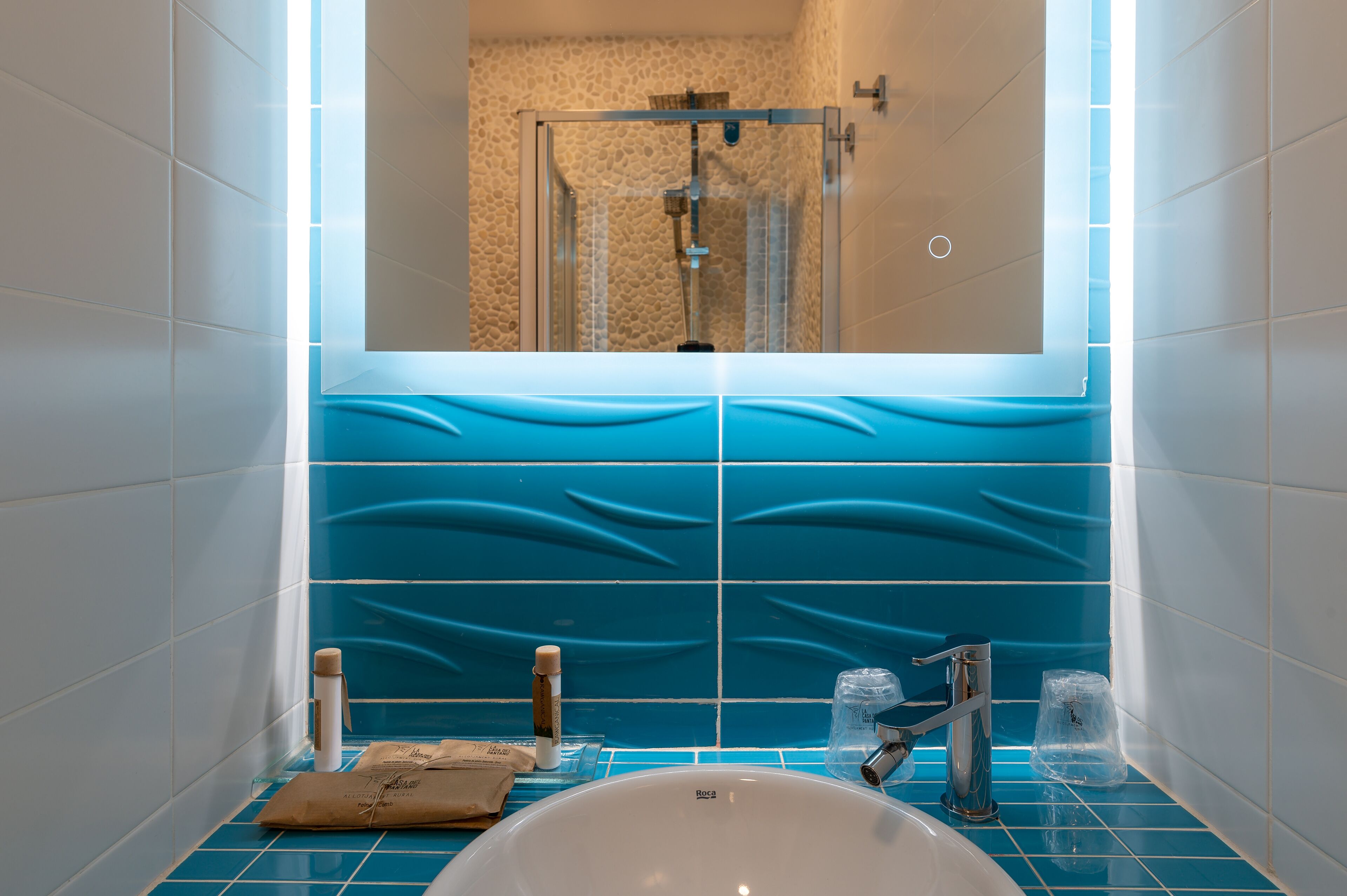 A bathroom with a white sink, blue tiles, a glass shower enclosure, and a mirror above the sink.