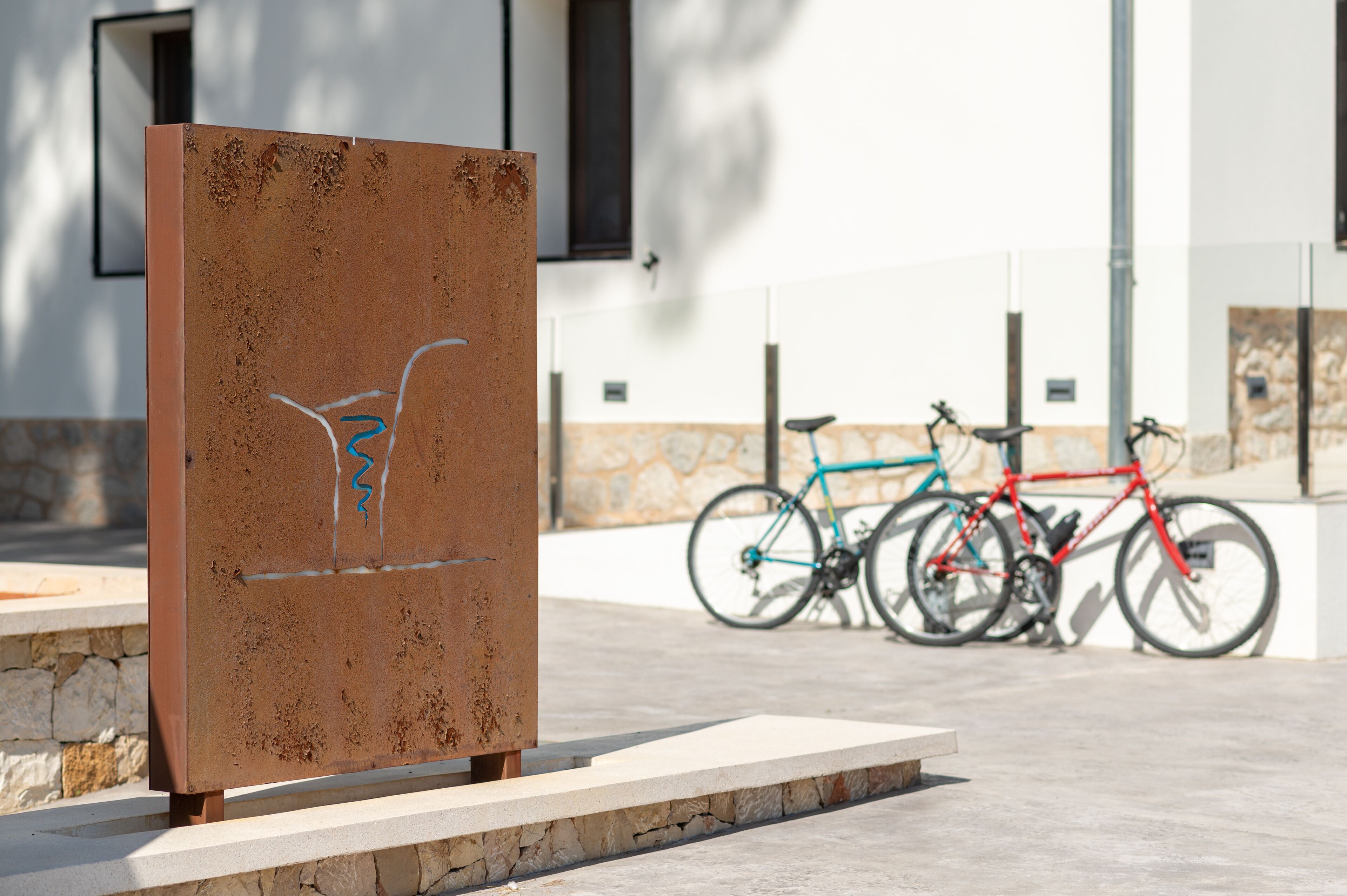 En skulptur av metall med graffiti, en röd cykel och en blå cykel som står lutade mot en byggnad med inslag av sten.