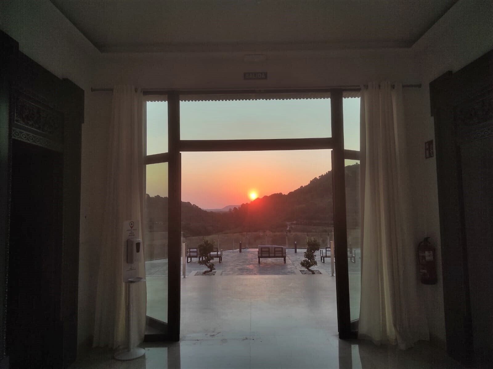 Una puerta abierta que da a una terraza con vistas al atardecer.