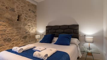 Un dormitorio con pared de piedra, cama con almohadillas azules y dos lámparas de noche.