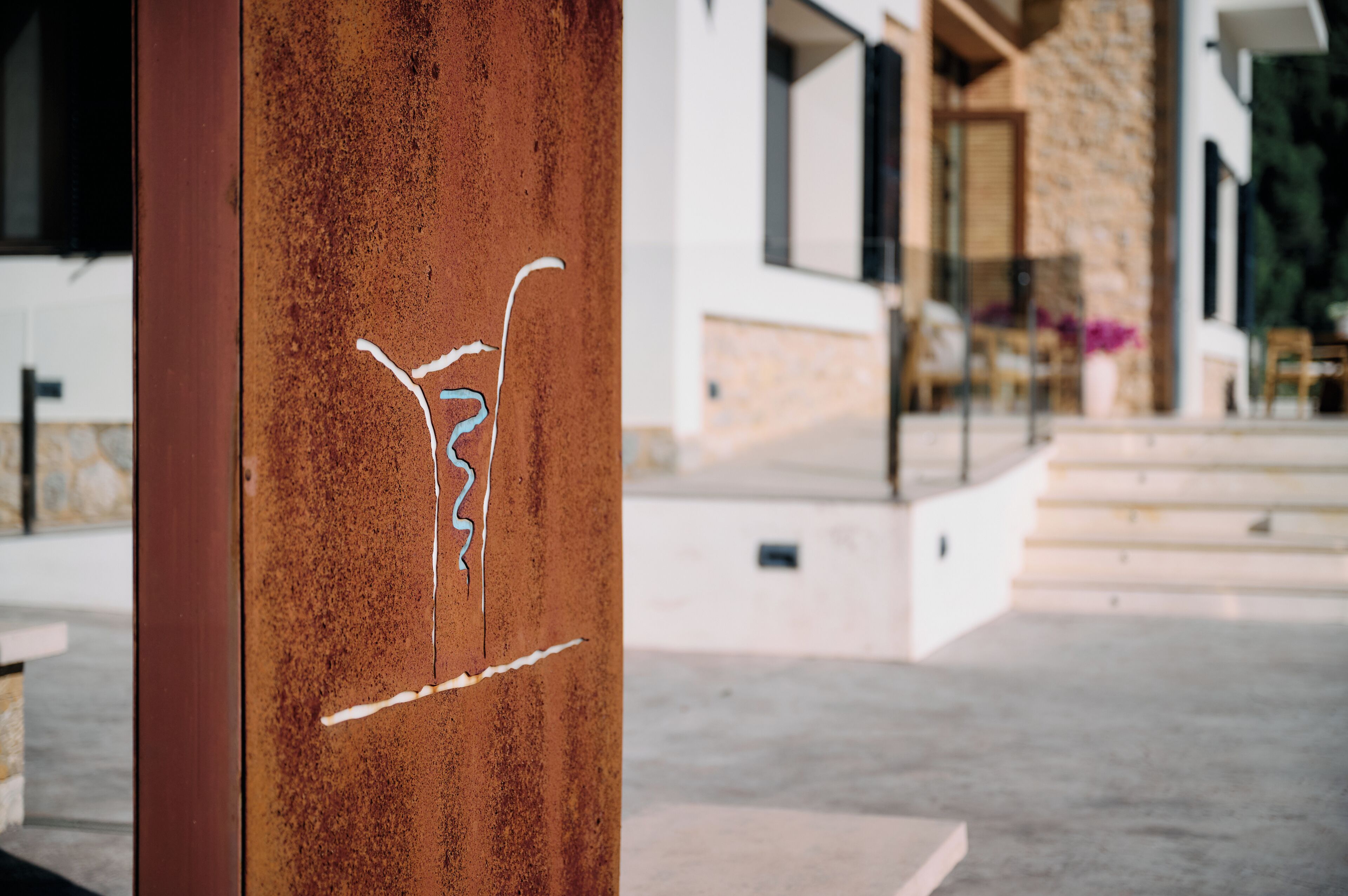 A rusted metal pillar with graffiti, a stone wall, and a modern building entrance with steps.