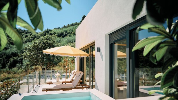Un'area piscina moderna all'aperto con poltrone a sdraio e ombrelloni, immersa nel verde e affacciata su una collina.