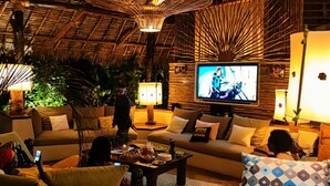 A cozy living room with a TV, comfortable seating, and a thatched ceiling.