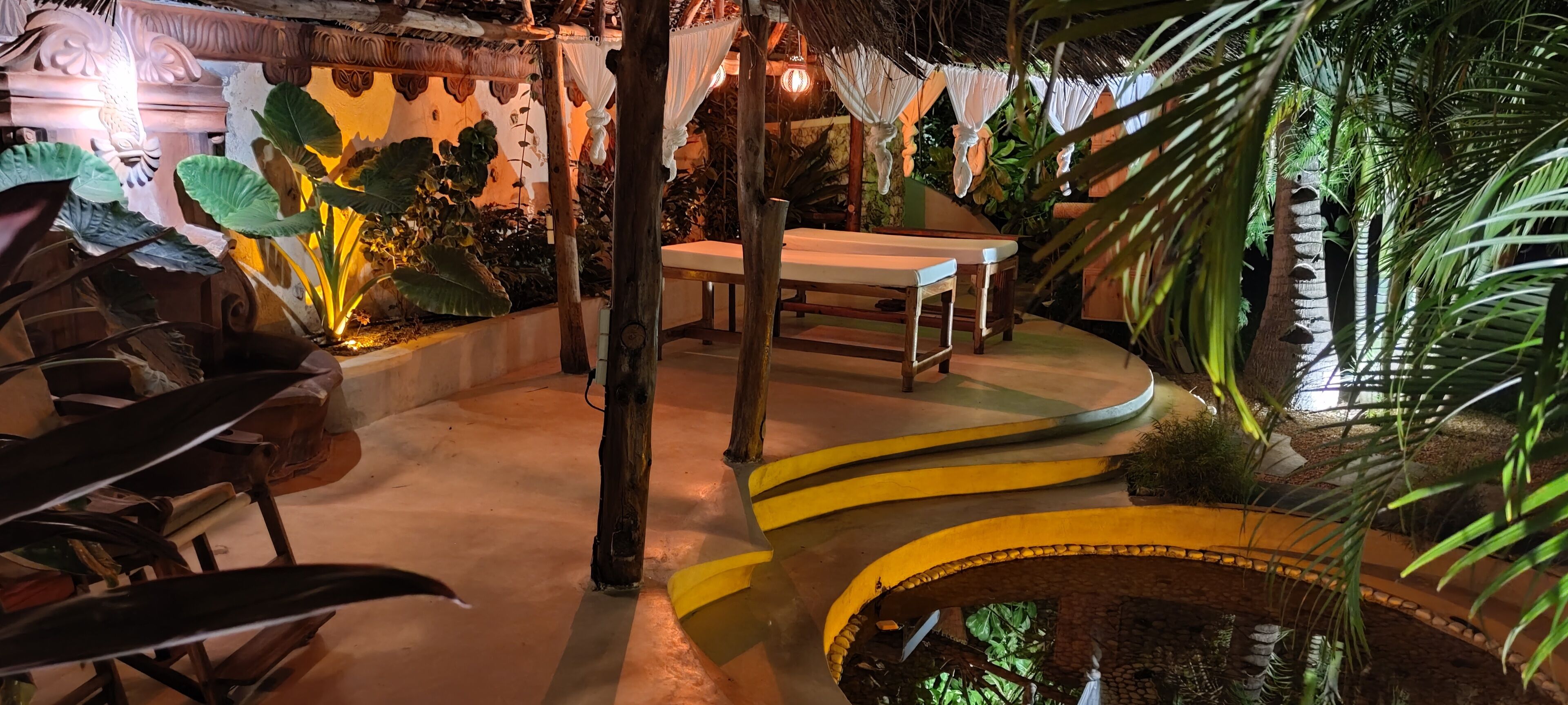 Ein tropisch gestalteter Raum mit einer gebogenen Sitzbank, einem kleinen Pool und üppiger Bepflanzung.