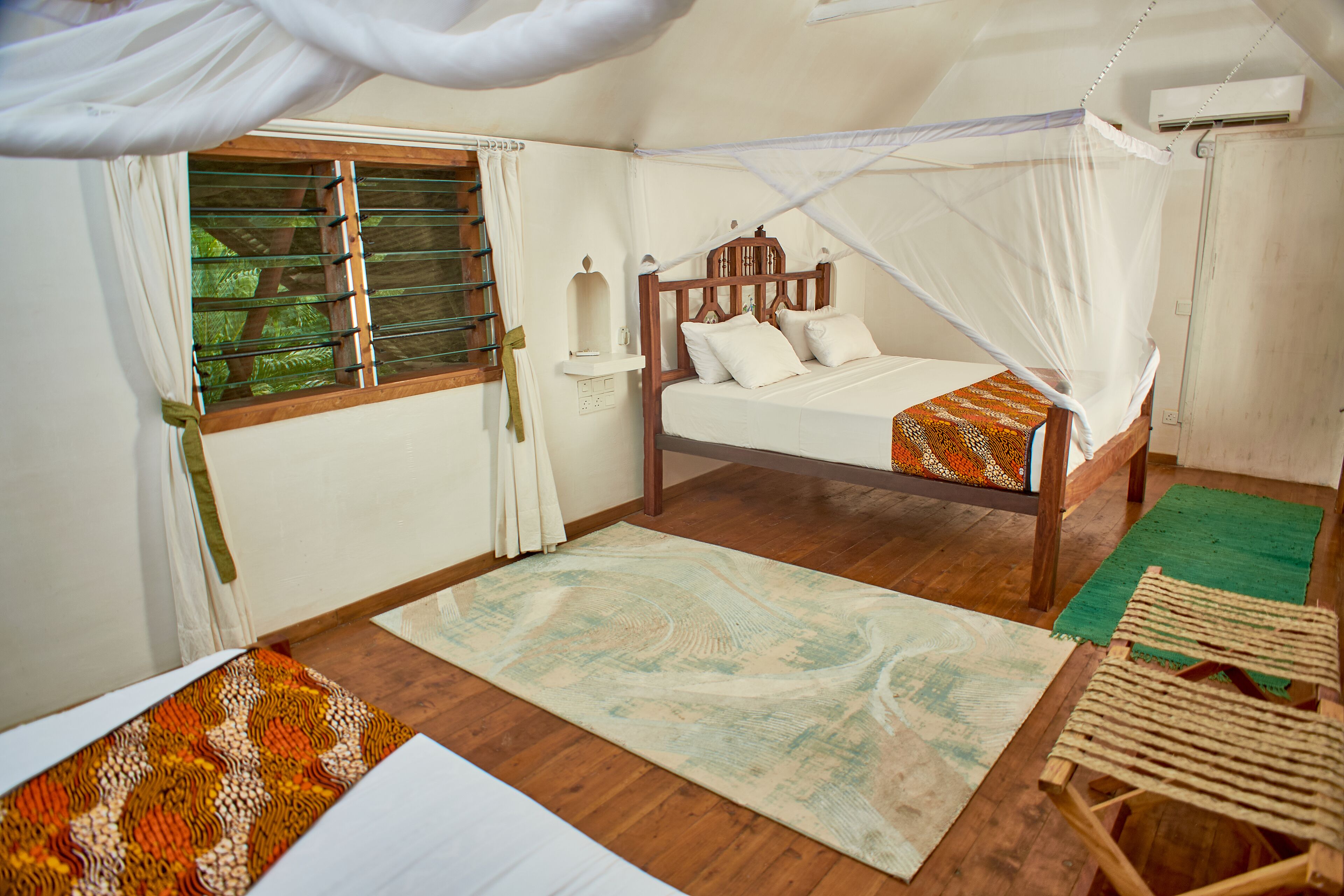 A bedroom with a wooden bed, a window with blinds, a green rug, and a wooden chair.