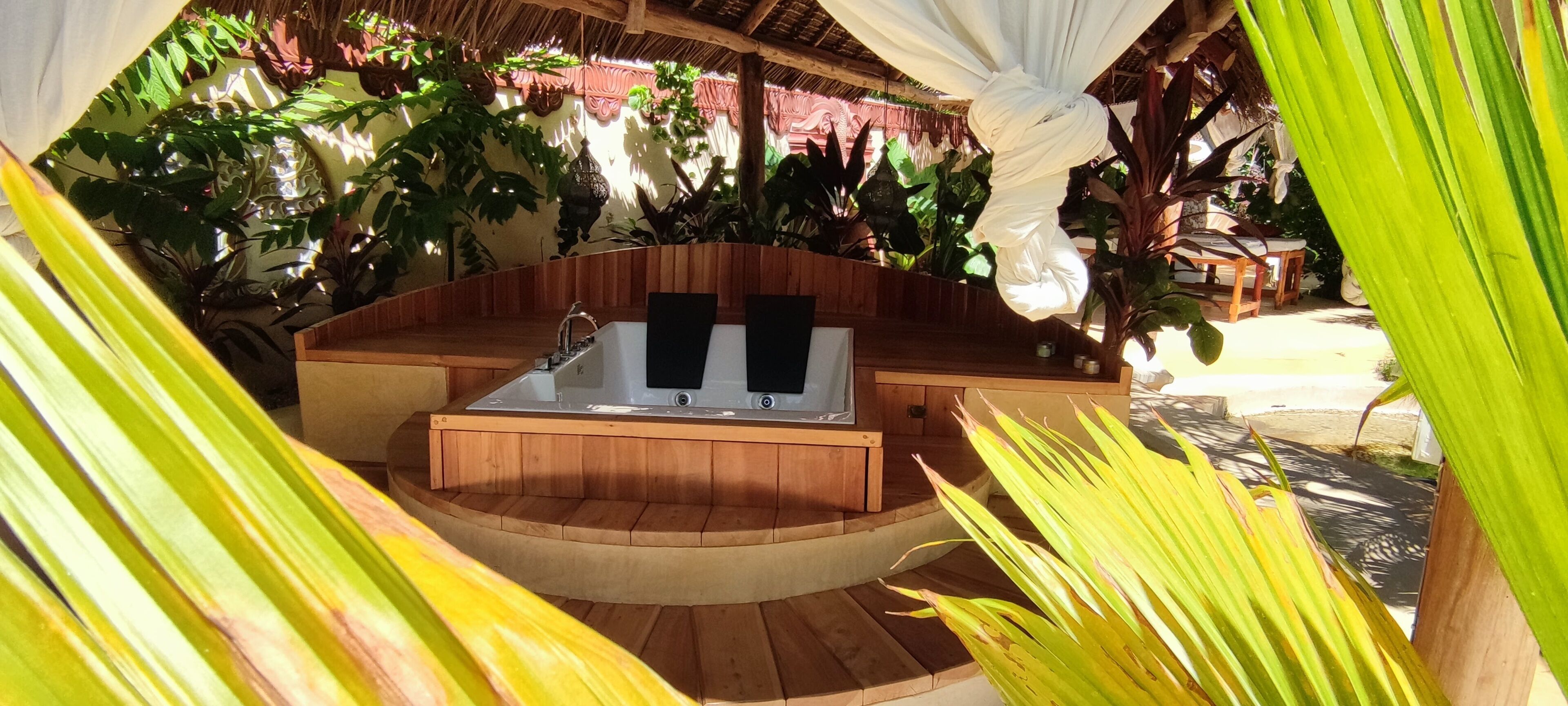 A hot tub in a wooden structure surrounded by tropical plants.