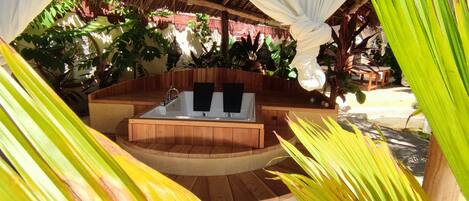 A hot tub in a wooden structure surrounded by tropical plants.